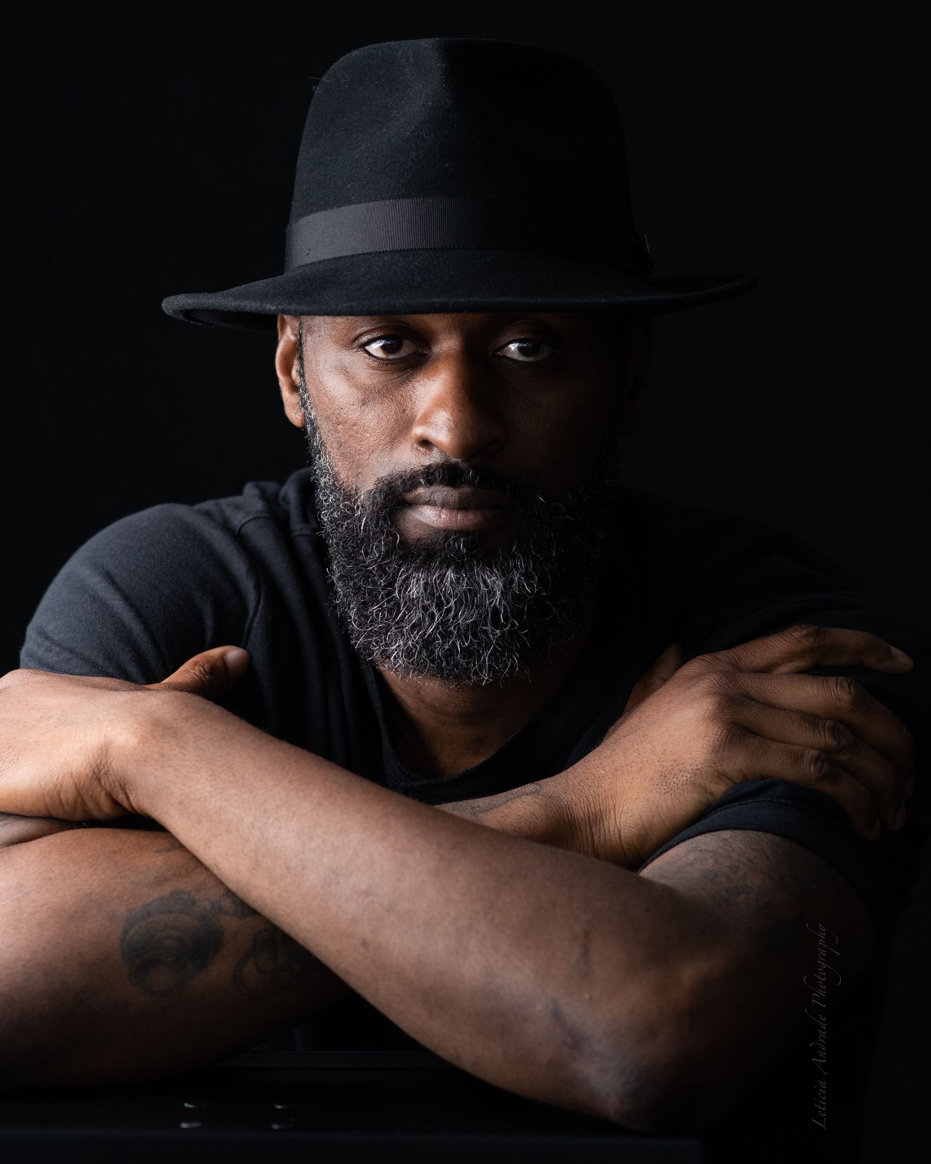 A man with a beard and a hat is sitting with his arms crossed.