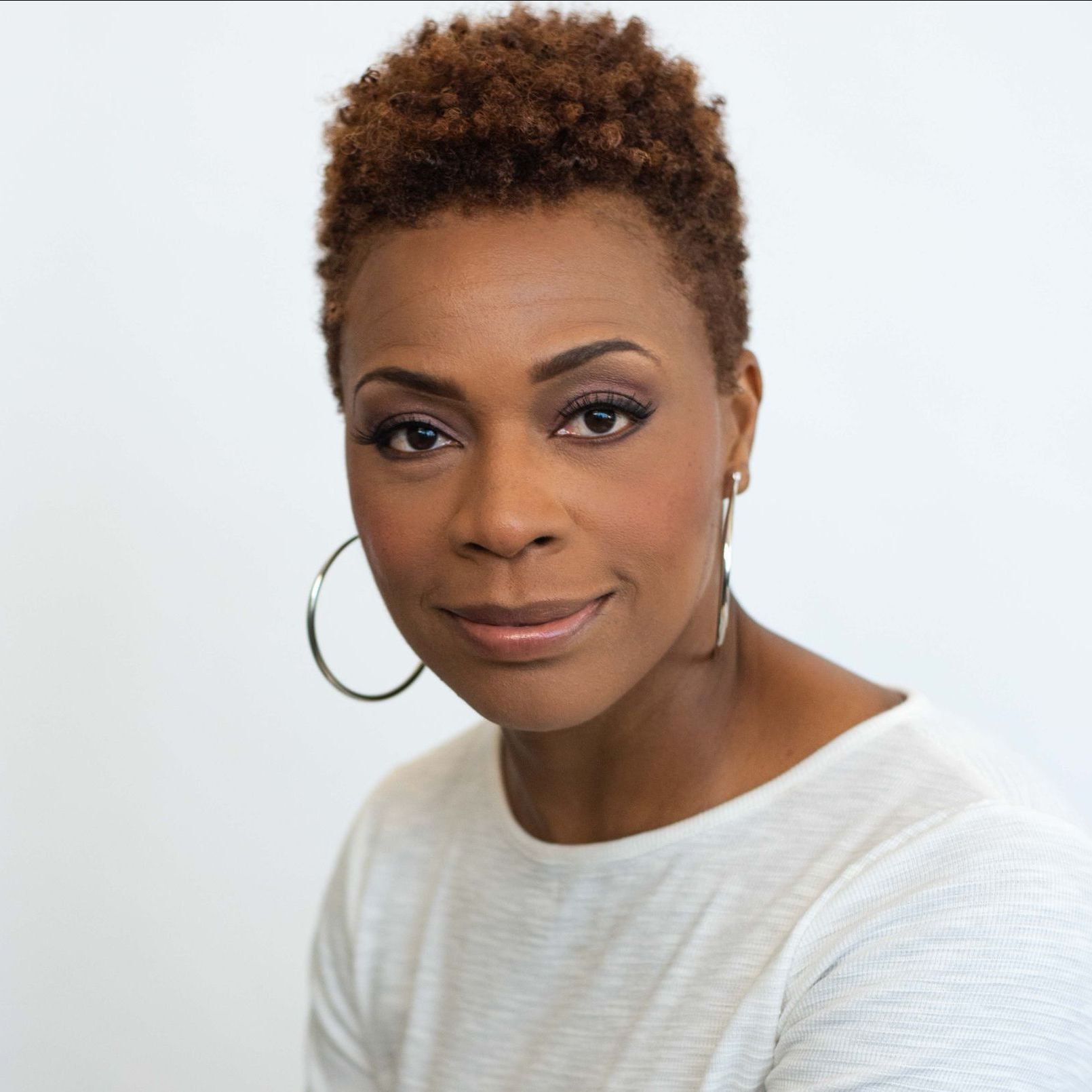 A woman wearing hoop earrings and a white shirt is smiling for the camera.