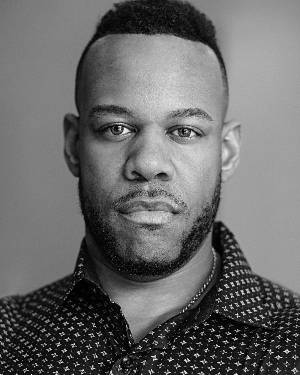 A black and white photo of a man with a beard wearing a polka dot shirt.
