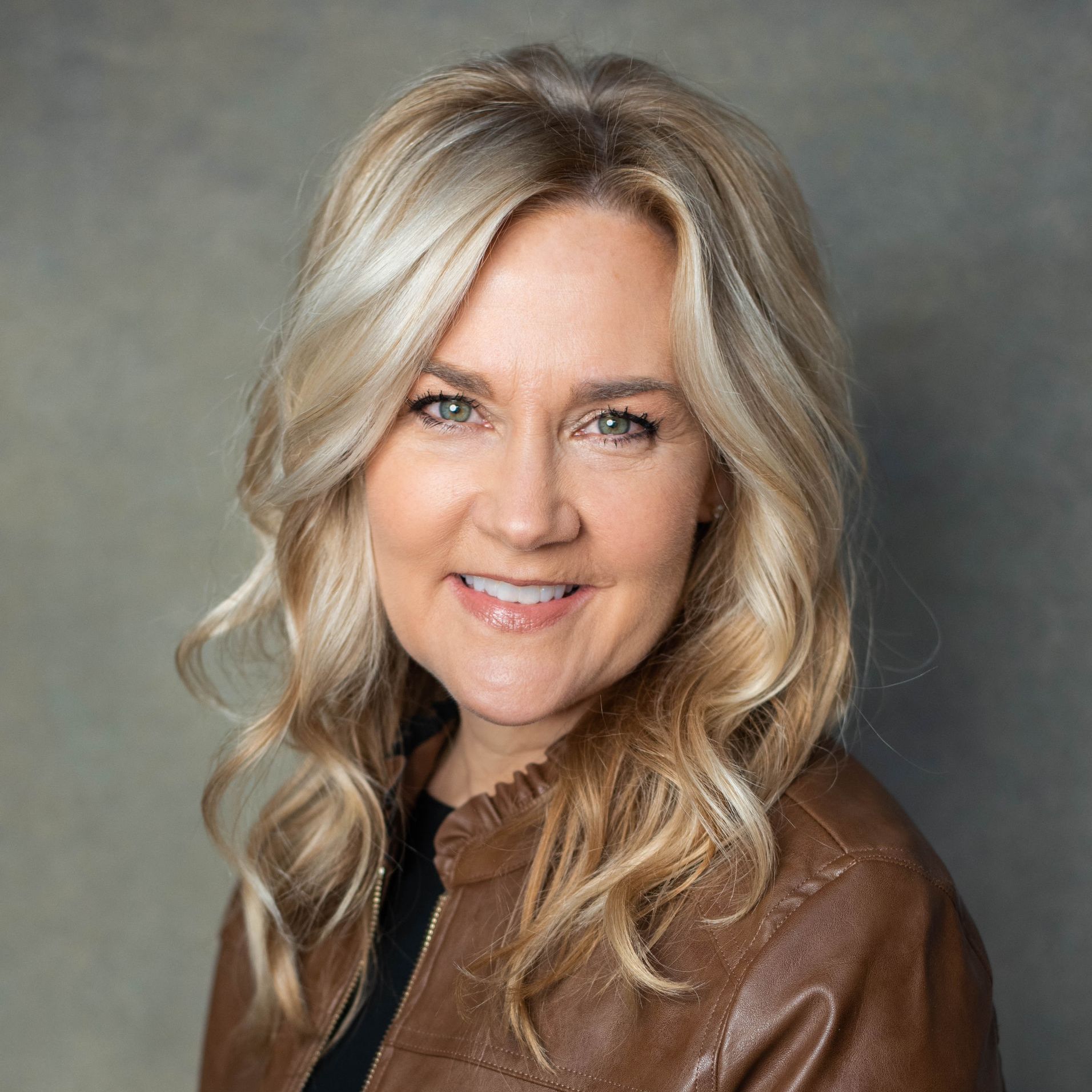 A woman is wearing a brown leather jacket and smiling for the camera.
