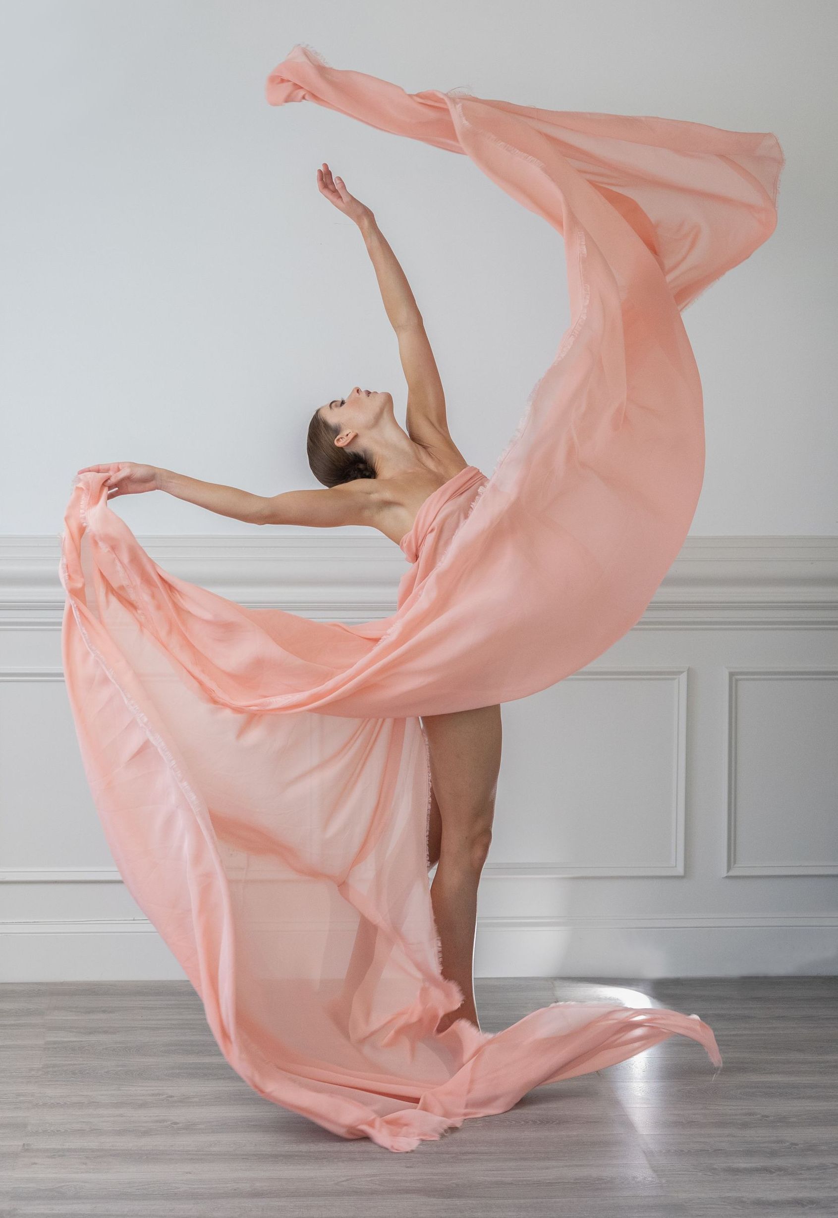 A woman in a long pink dress is dancing in a room.