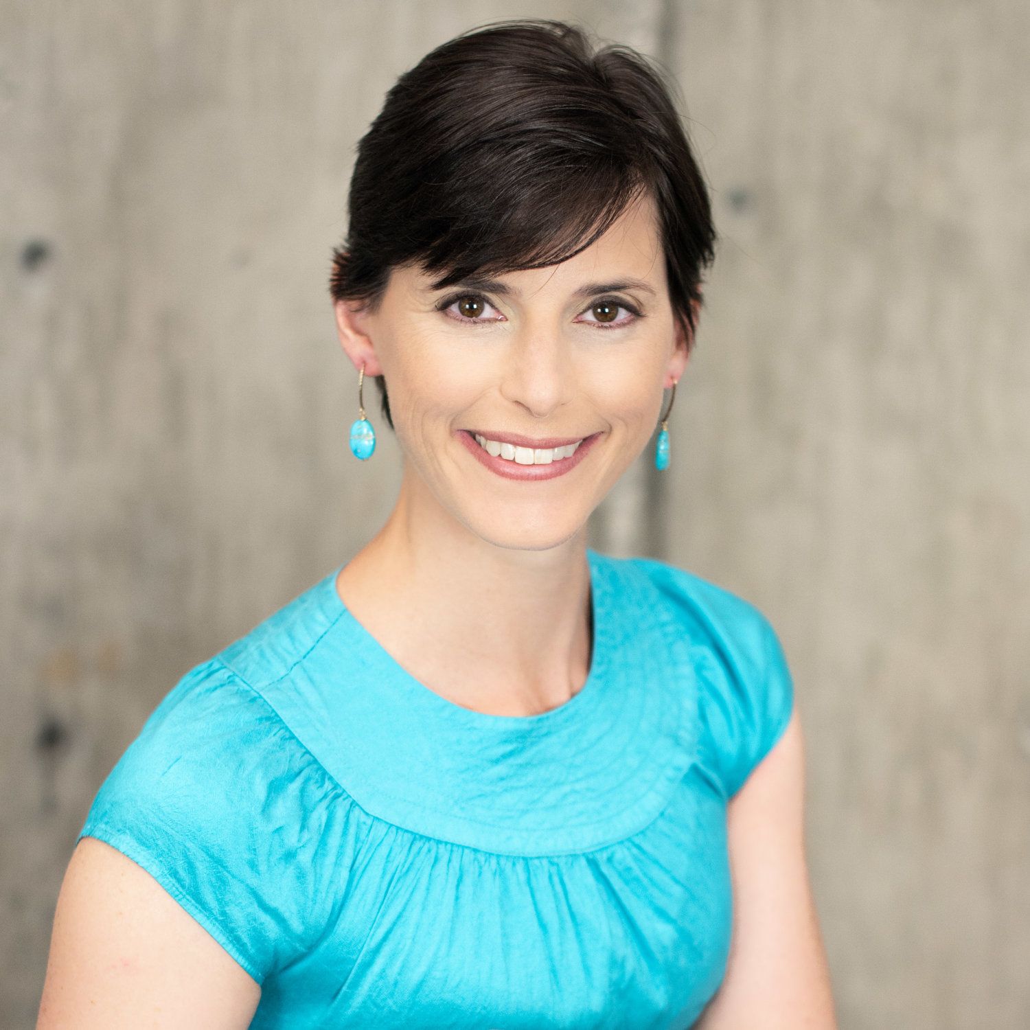 A woman wearing a blue shirt and earrings smiles for the camera