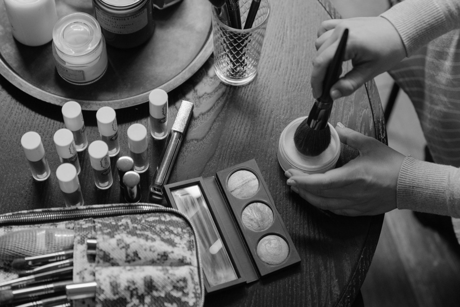 Several makeup palettes are on a table with a vase of flowers in the background