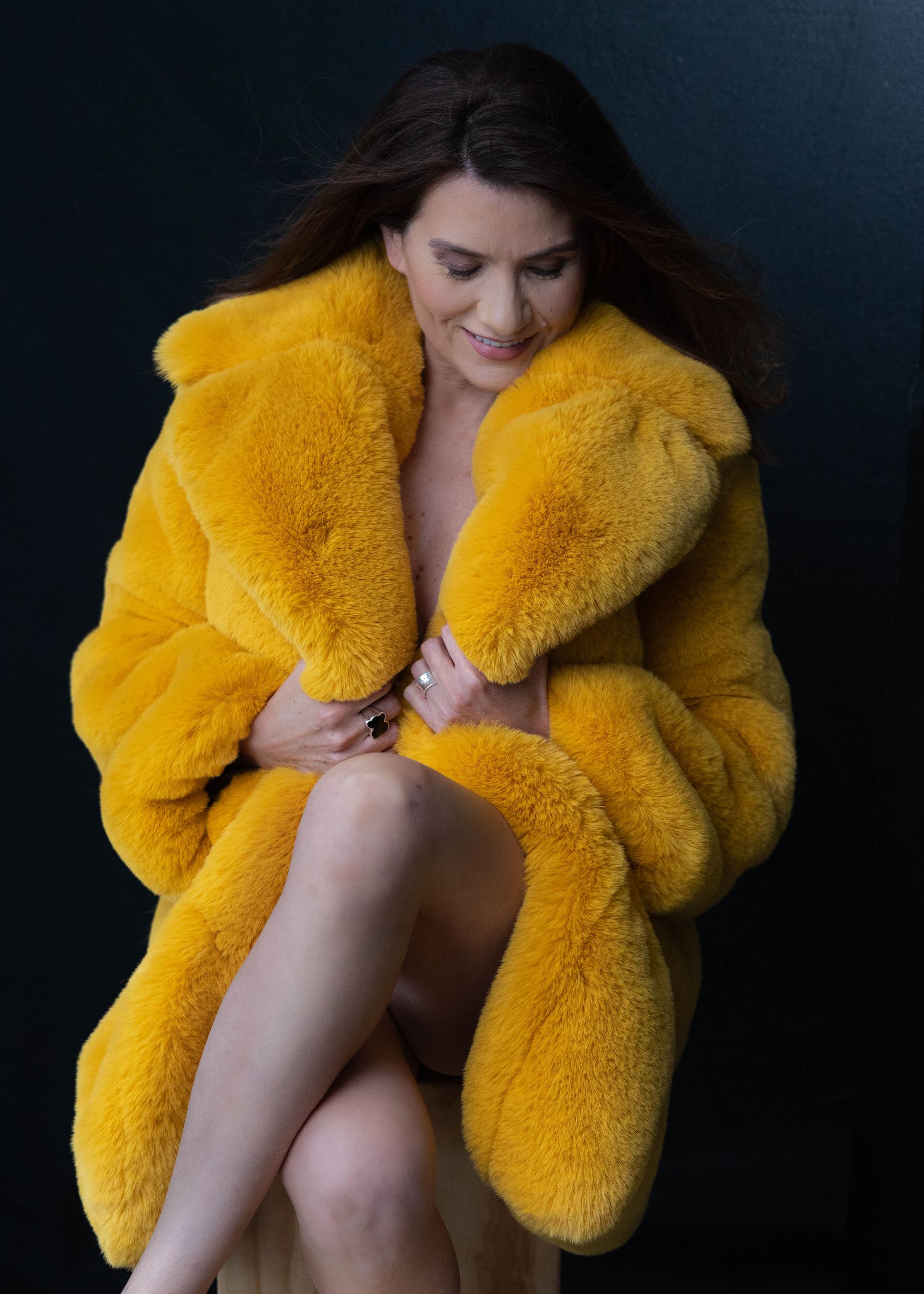 A woman is sitting on a chair wearing a yellow fur coat.