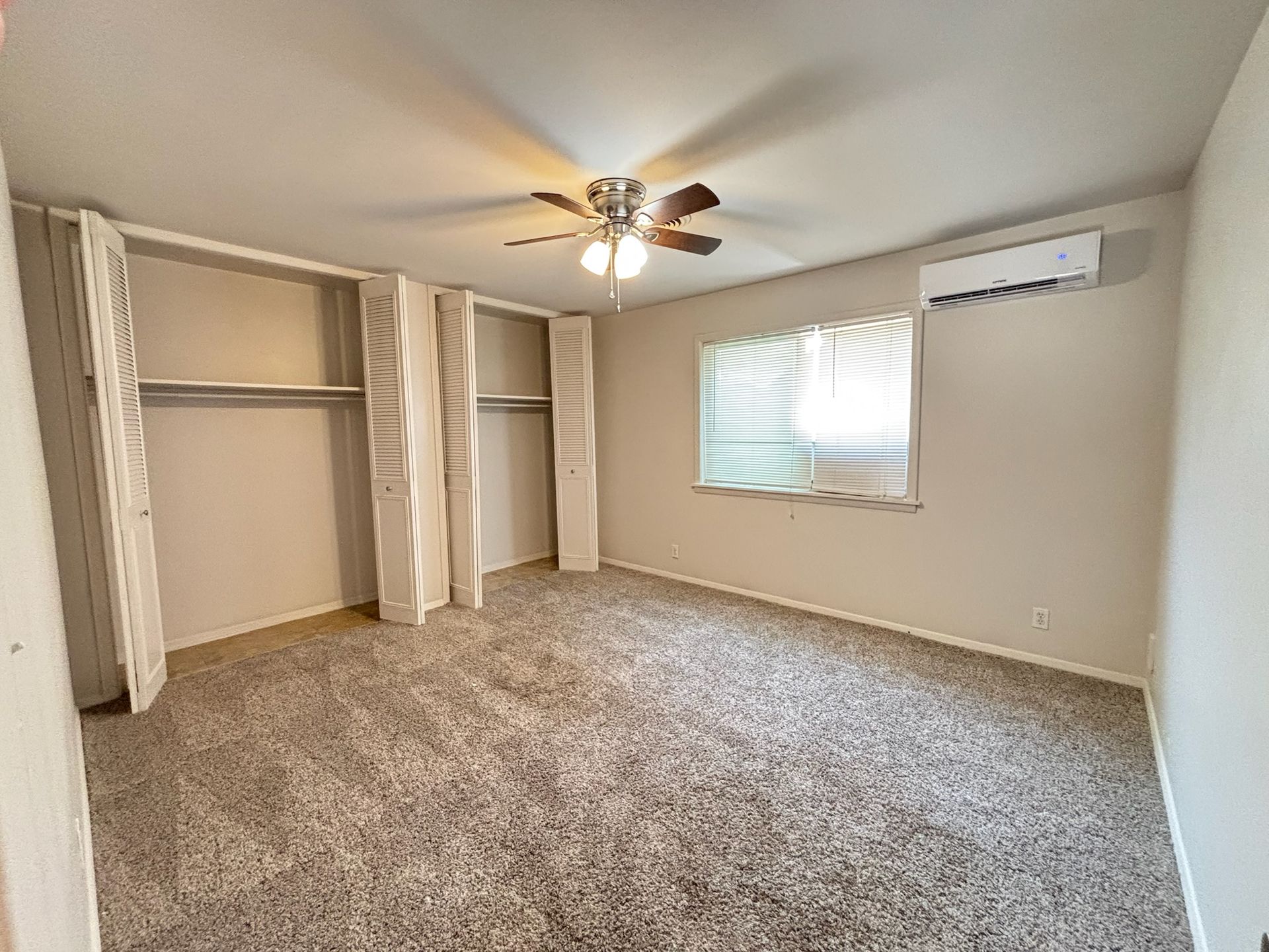 An empty bedroom with a ceiling fan and a window.