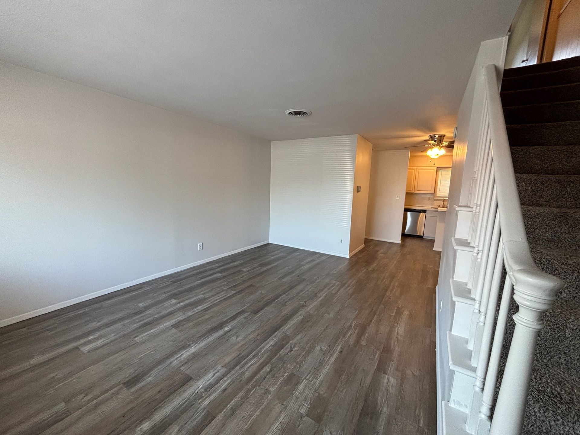 An empty living room with hardwood floors and stairs leading to the kitchen.