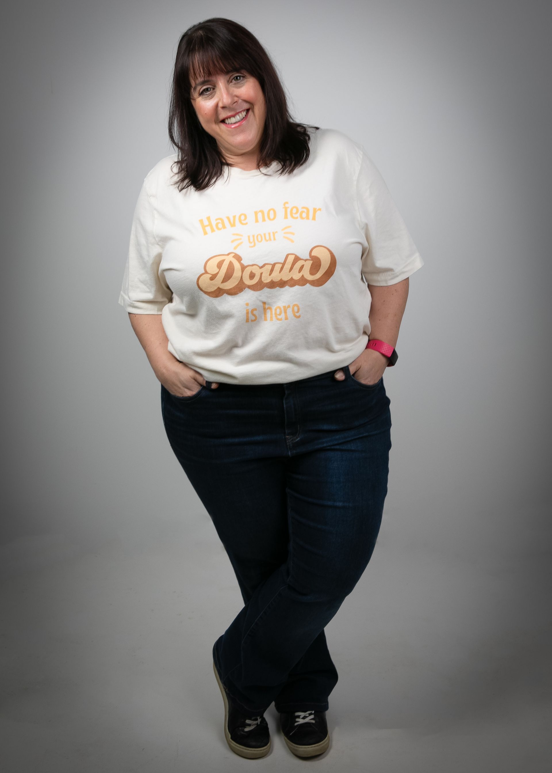 Jennifer Tawil is smiling while wearing a shirt that says your doula is here before she meets with a postpartum client.
