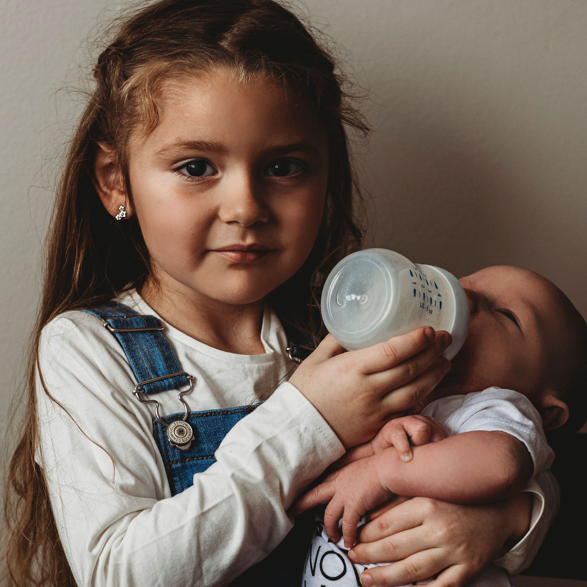A little girl is feeding a baby from a bottle.