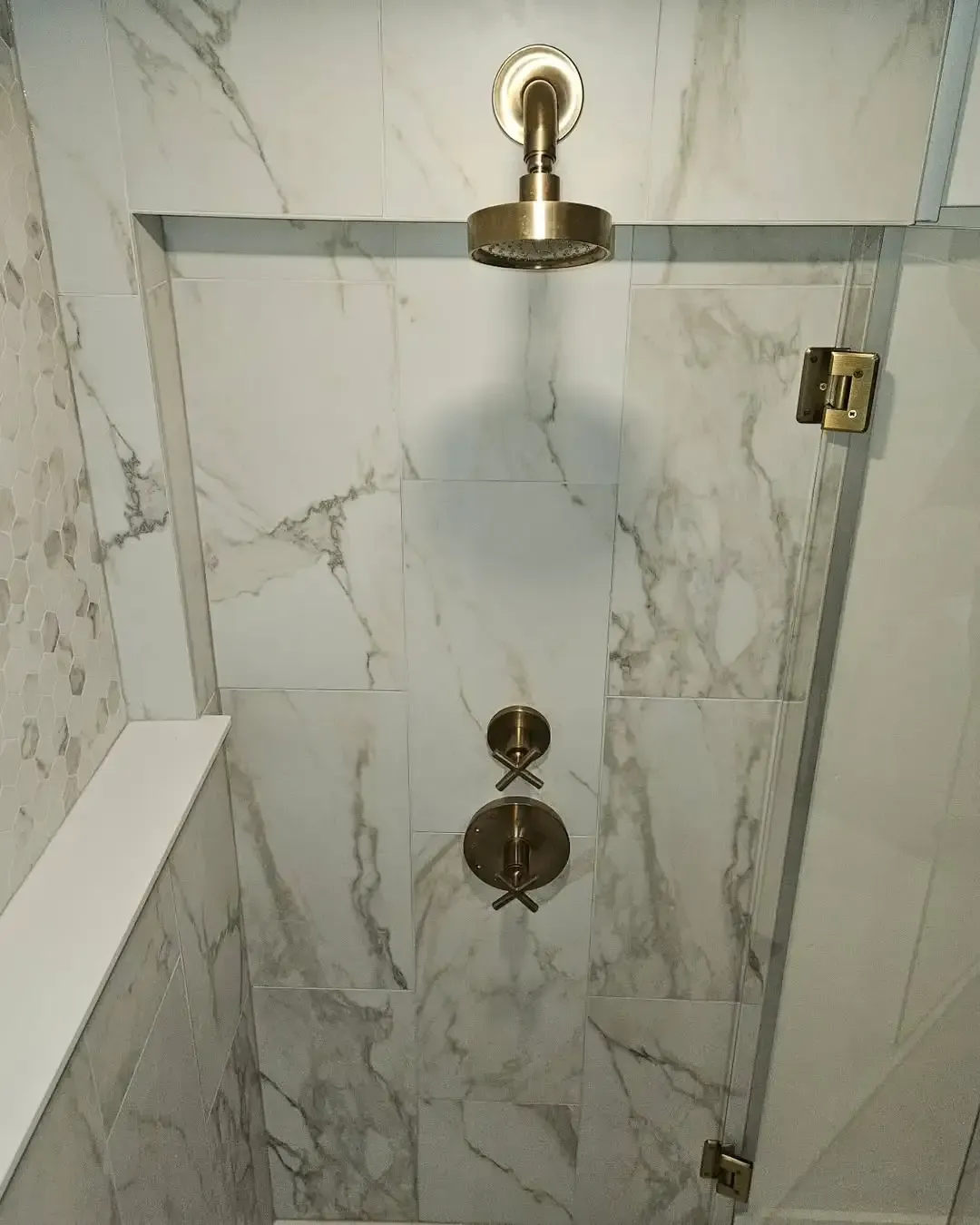 A shower stall with marble tiles and a brass shower head