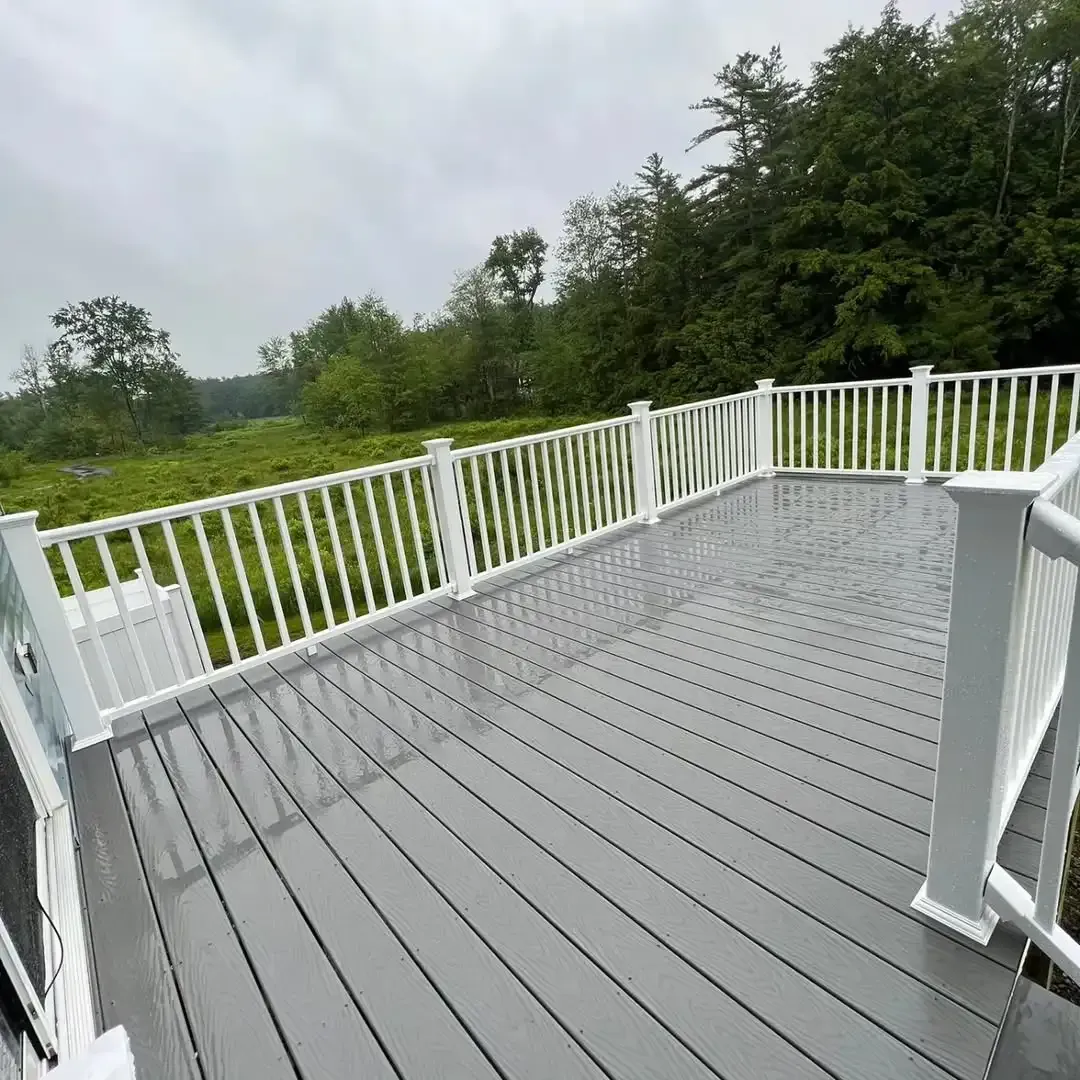 A gray deck with a white railing and trees in the background.