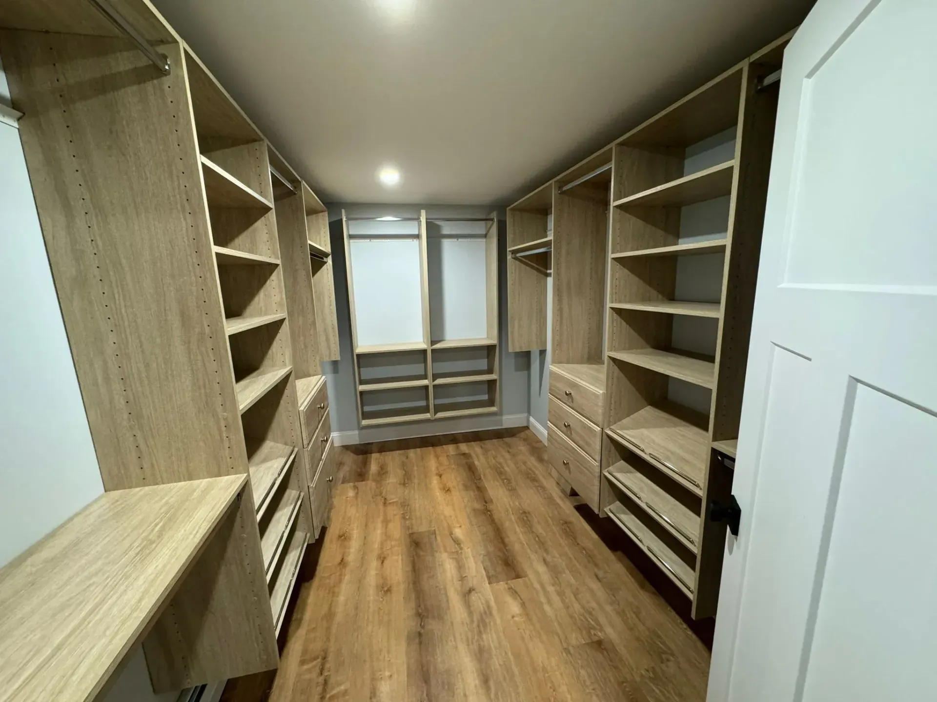A large walk in closet with wooden shelves and drawers.