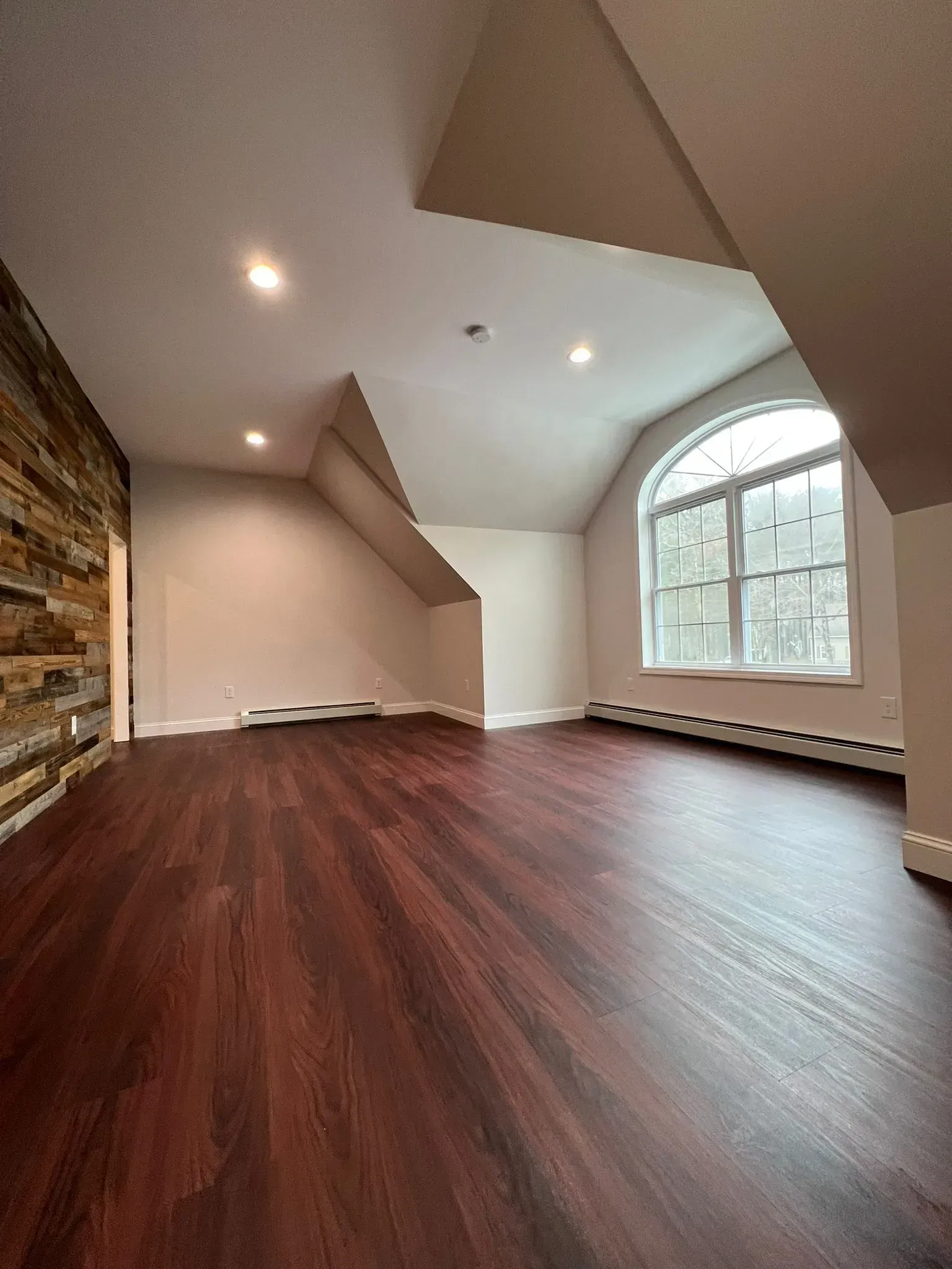 An empty room with hardwood floors and a large window.