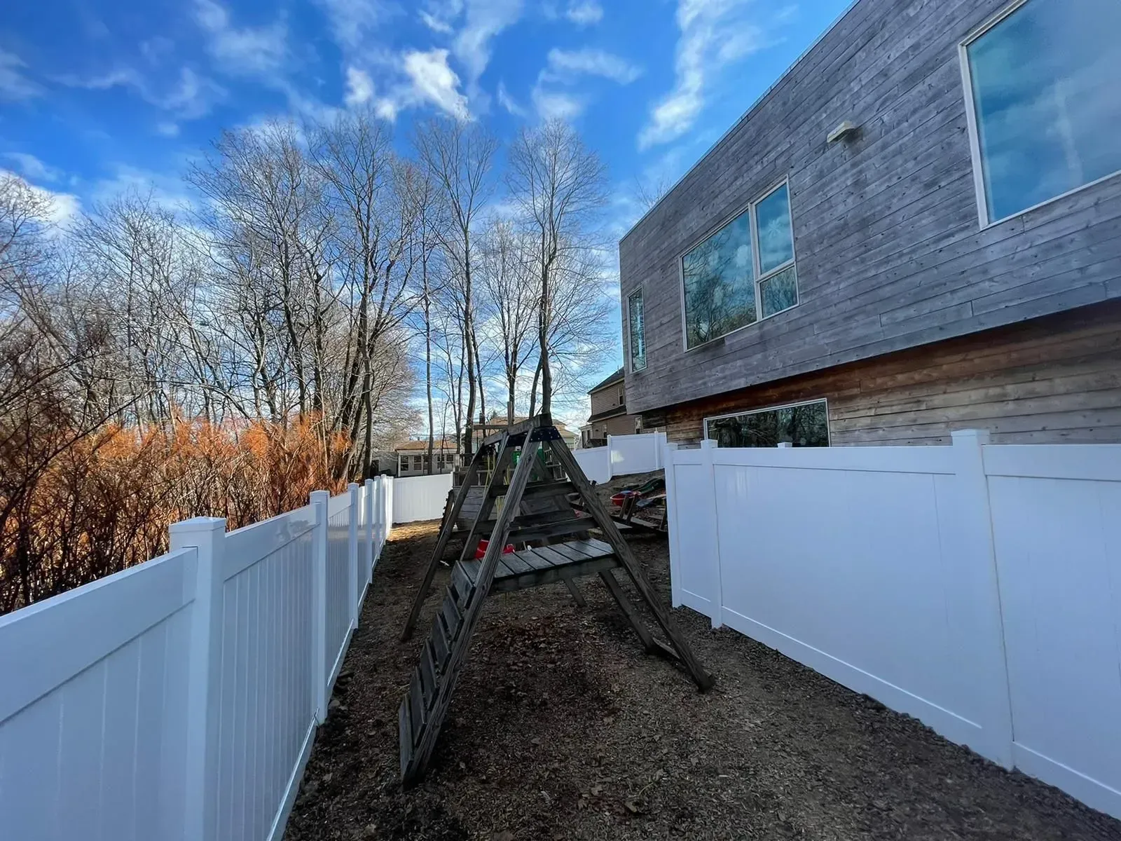 A white fence surrounds a playground in front of a house.
