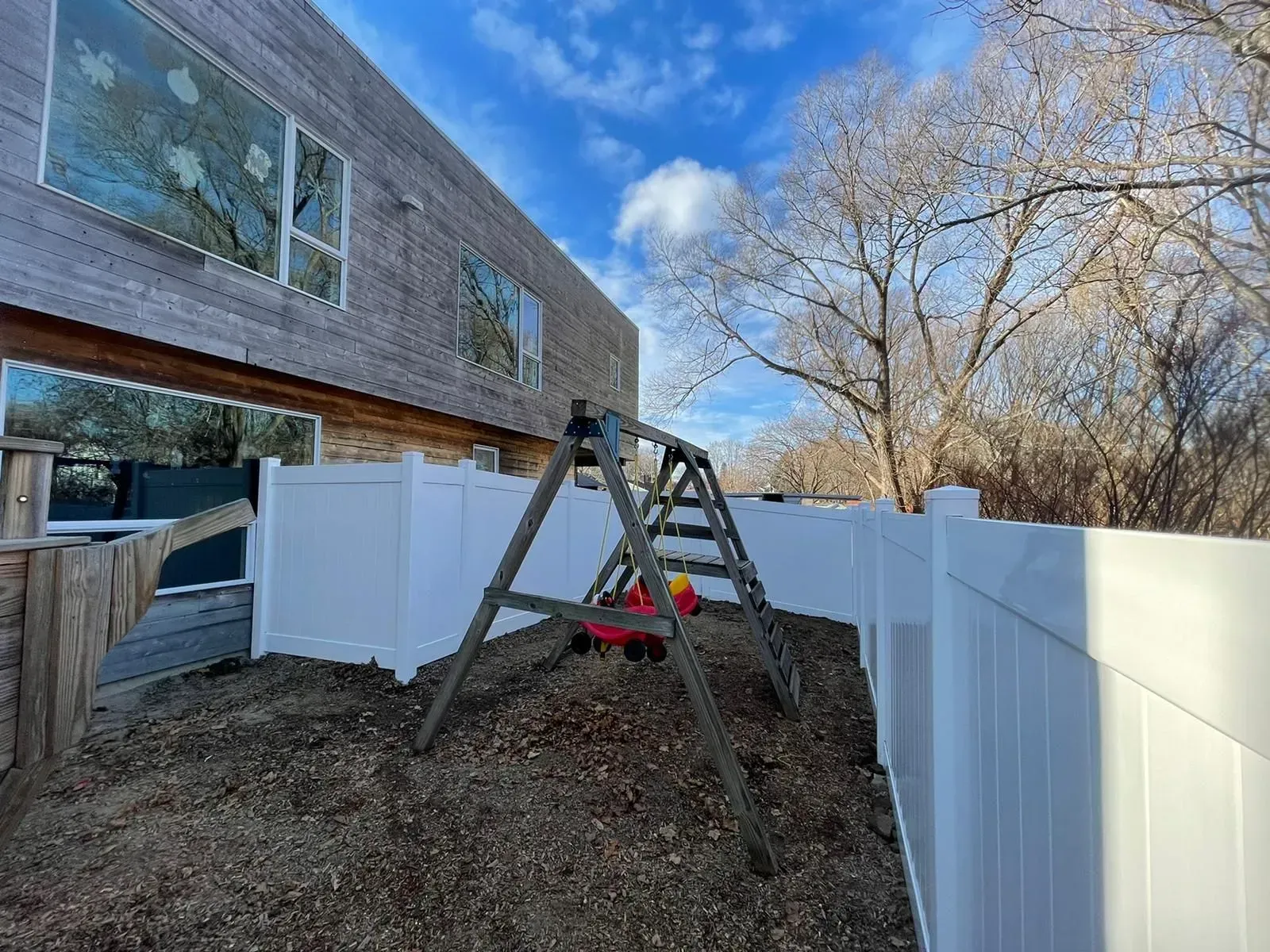 A backyard with a swing set and a white fence.