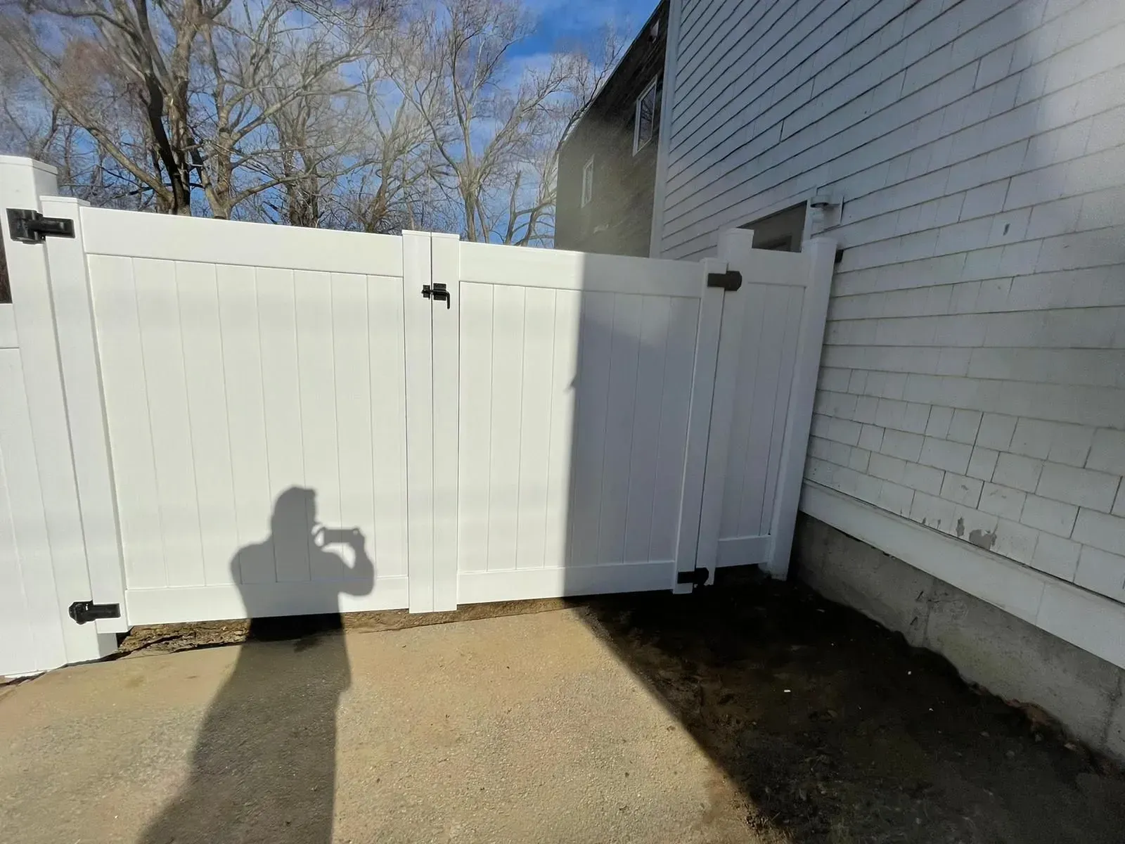 A person is taking a picture of a white fence in front of a house.