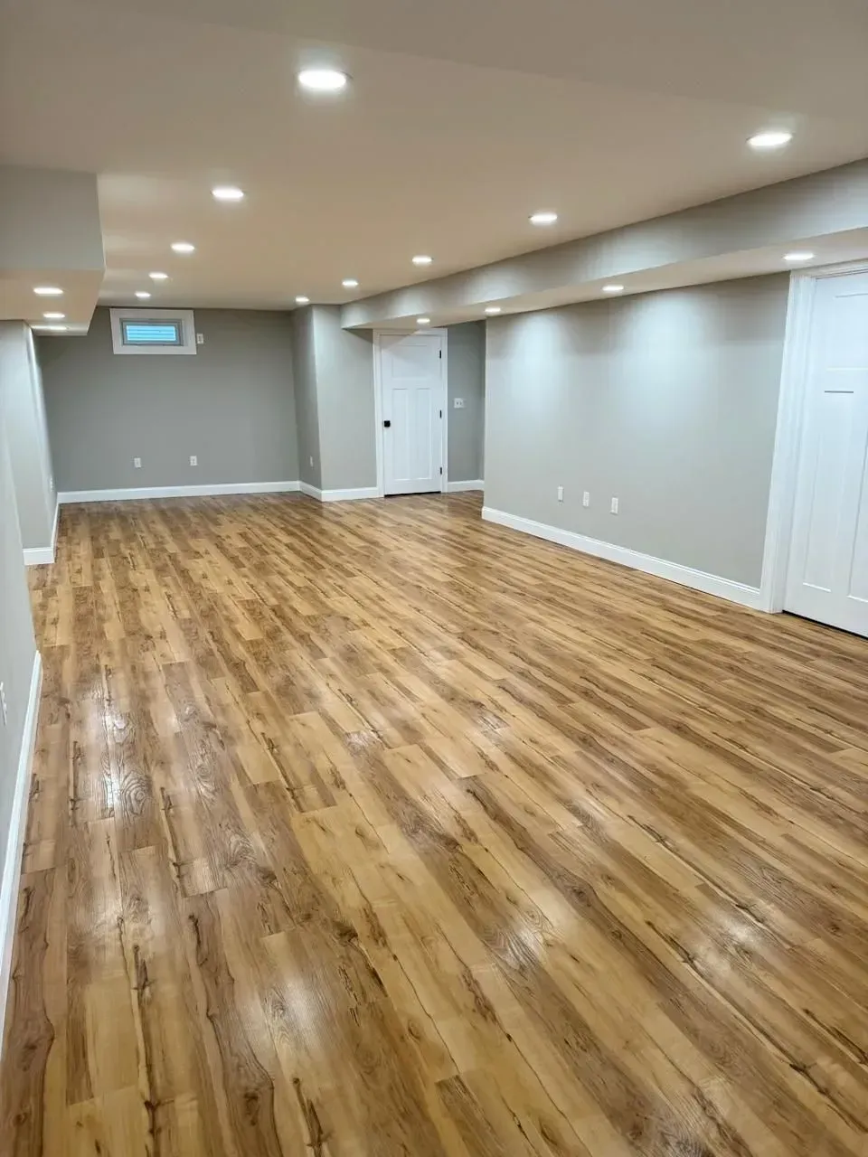 A large empty basement with hardwood floors and gray walls.