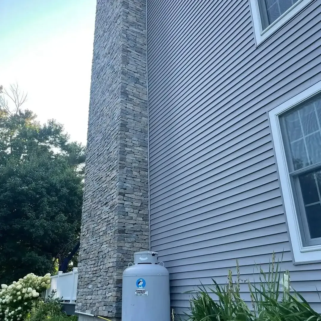 A propane tank is sitting on the side of a house next to a chimney.