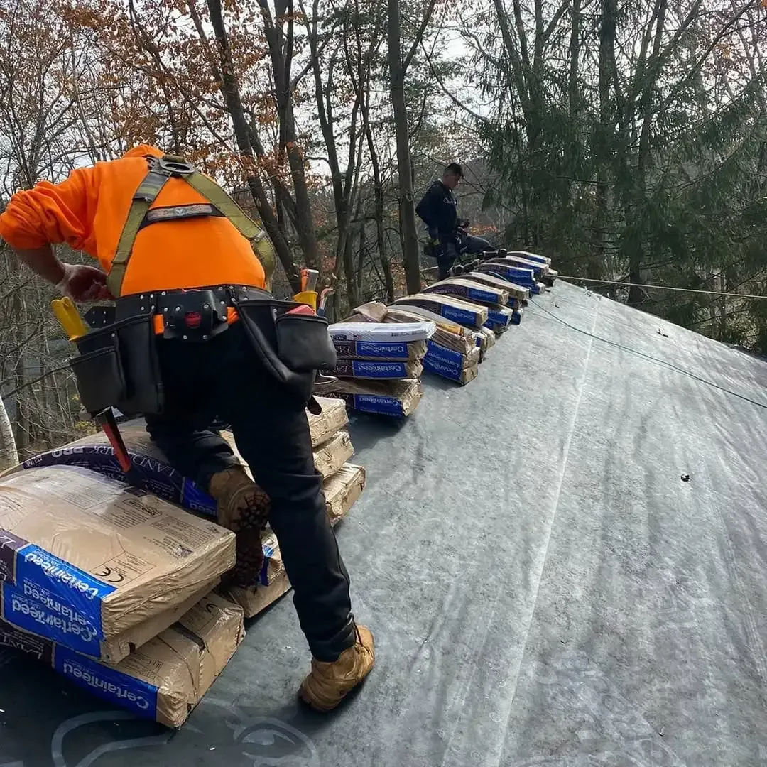 A man in an orange shirt is standing on a roof with bags of cement.