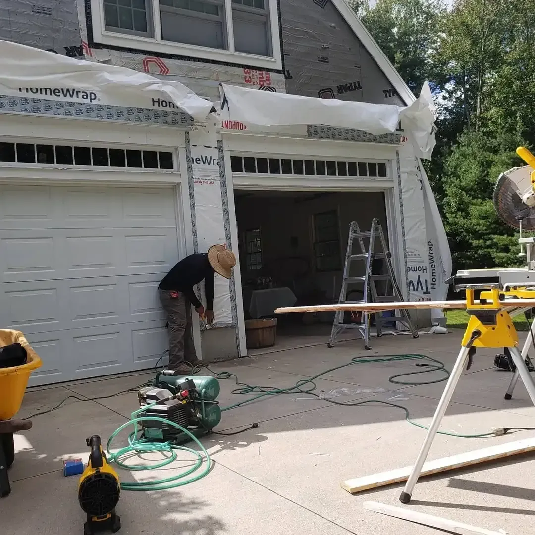 A man is cutting a piece of wood in front of a garage door.