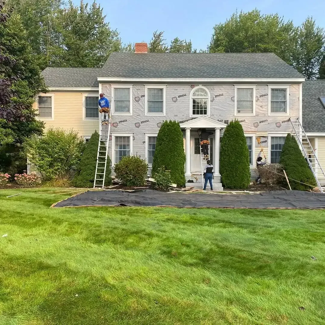 A man is standing on a ladder in front of a large house.