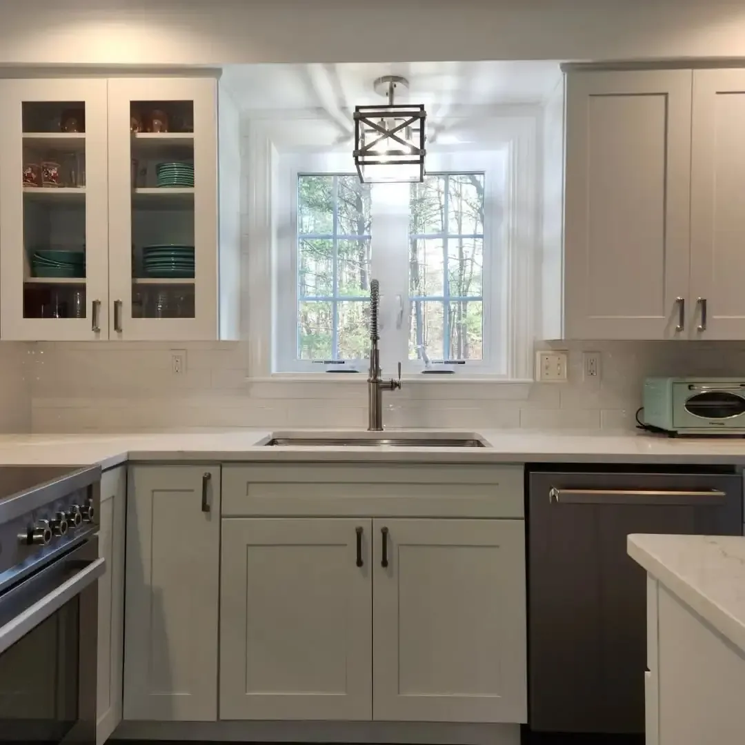 A kitchen with white cabinets , a stove , a sink , and a window.