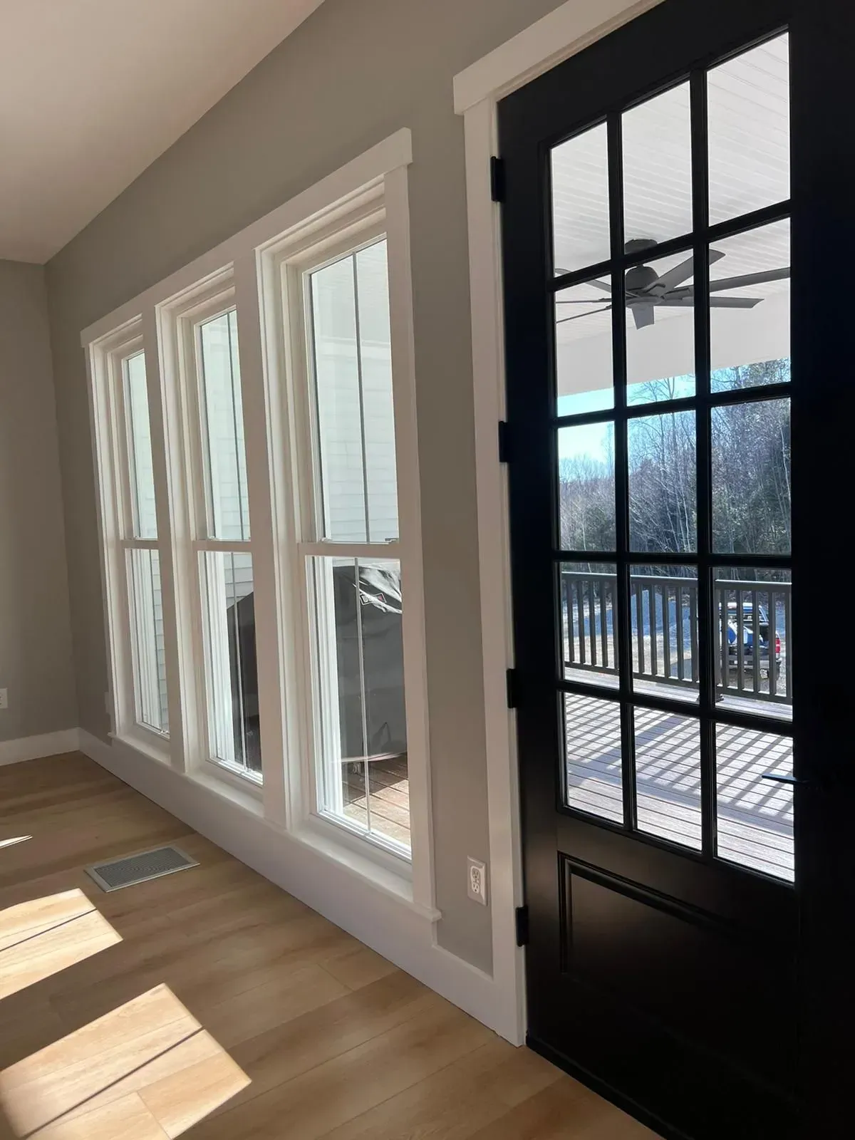A room with a lot of windows and a black door leading to a balcony.