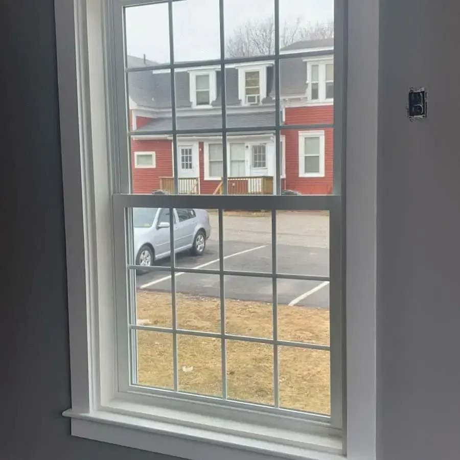 A window with a view of a red house and a parking lot.