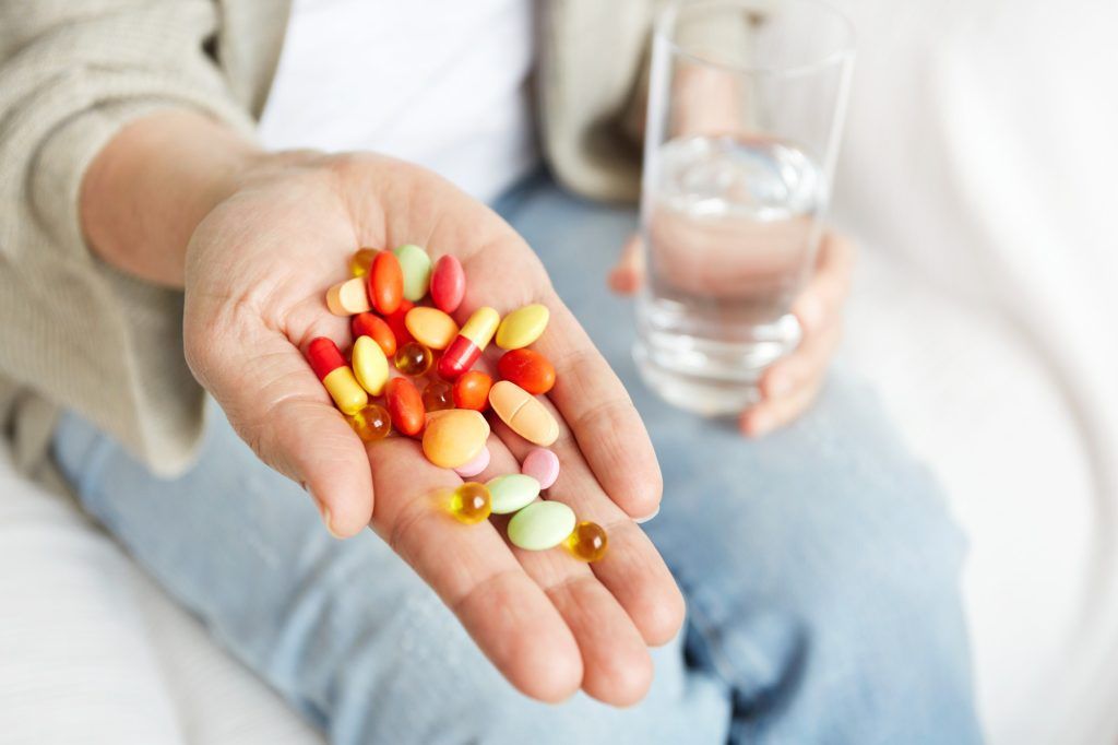 Person holding a handful of colorful pills and a glass of water.