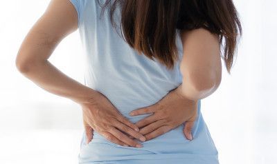 Woman in light blue shirt, hands on lower back, likely experiencing back pain.
