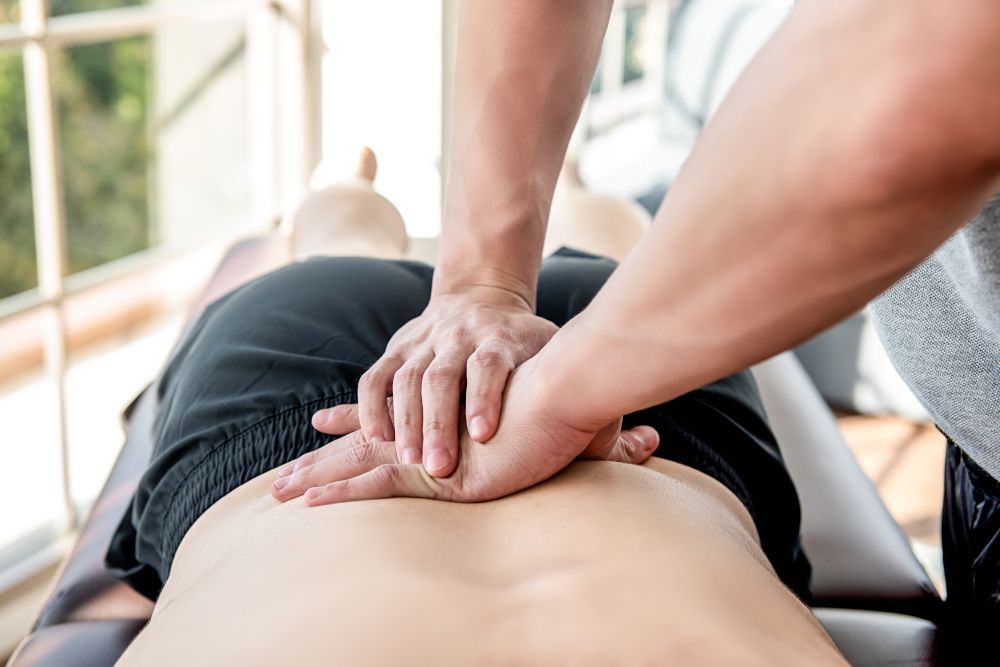 Hands giving a back massage to someone lying face down on a massage table.