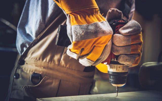 Person wearing work gloves drilling into material.