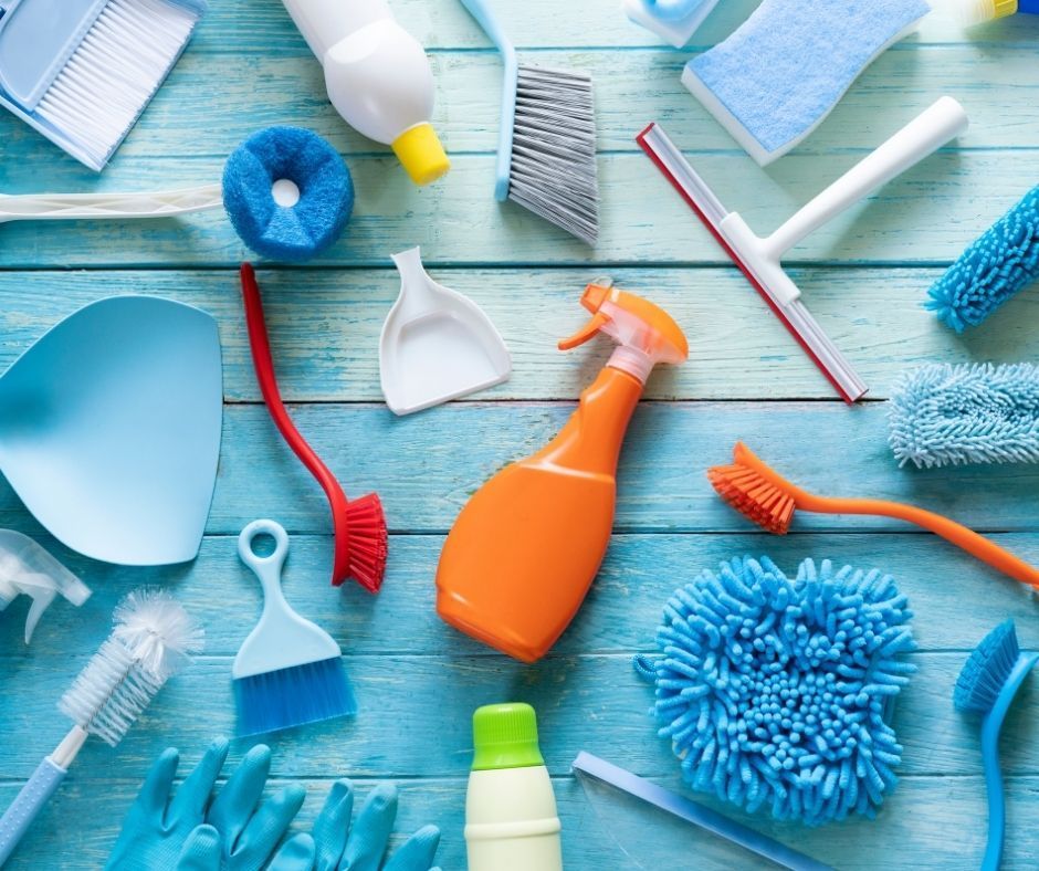 Cleaning supplies arranged on a blue wooden surface. Includes spray bottles, brushes, sponges, and gloves.