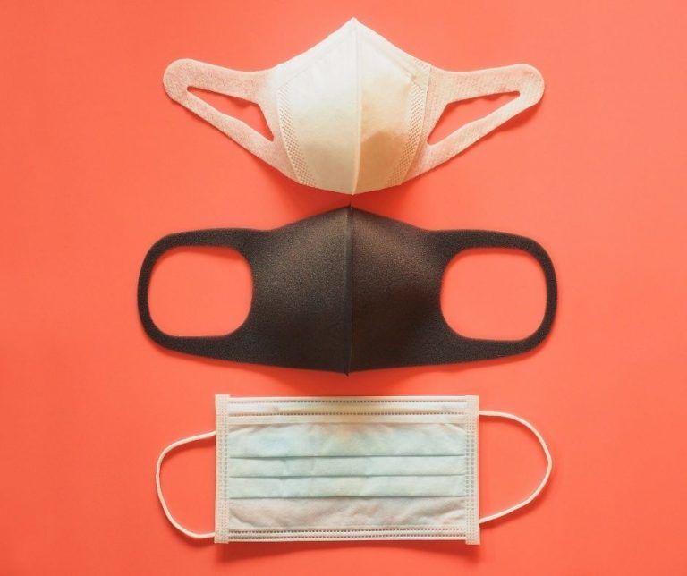 Three face masks, white, black, and blue, on a red background.