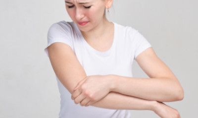 Woman in white shirt, clutching elbow in pain, showing facial discomfort.