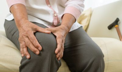 Person holding their knees, showing pain; cane nearby on sofa.