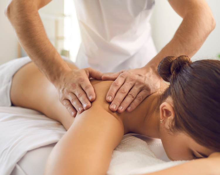 Massage therapist giving back massage to a woman lying face down on a massage table.