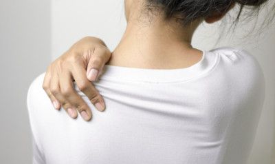 Woman in white shirt touching her shoulder, possibly in pain.