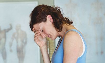 Woman with head in hand, looking down, possibly in pain, in a light-filled room.