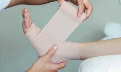 Person wrapping an ankle with a beige bandage.