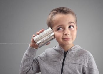 Boy with tin can phone looks up, smiling slightly.