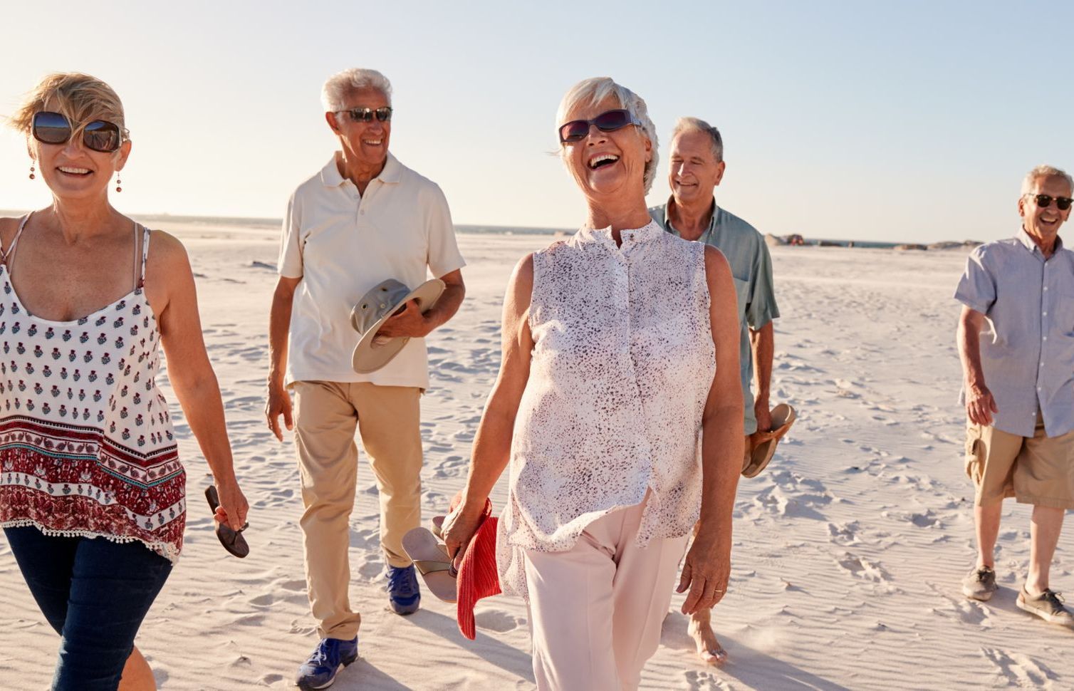 Group of smiling seniors walking on a beach, enjoying a sunny day.