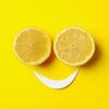 Two lemon halves arranged as eyes with a paper smile on a yellow background.