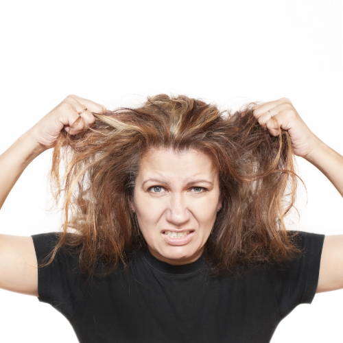 Woman with tangled hair, grimacing, pulling hair in frustration.
