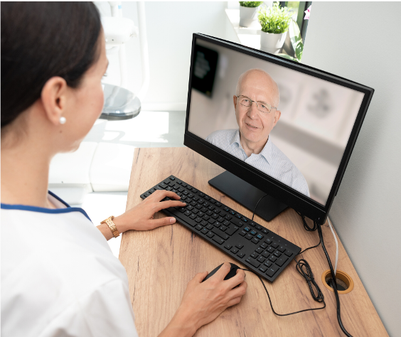 A medical professional in white scrubs on a video call with an elderly man.