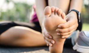 Woman sitting, holding foot, possibly in pain outdoors.