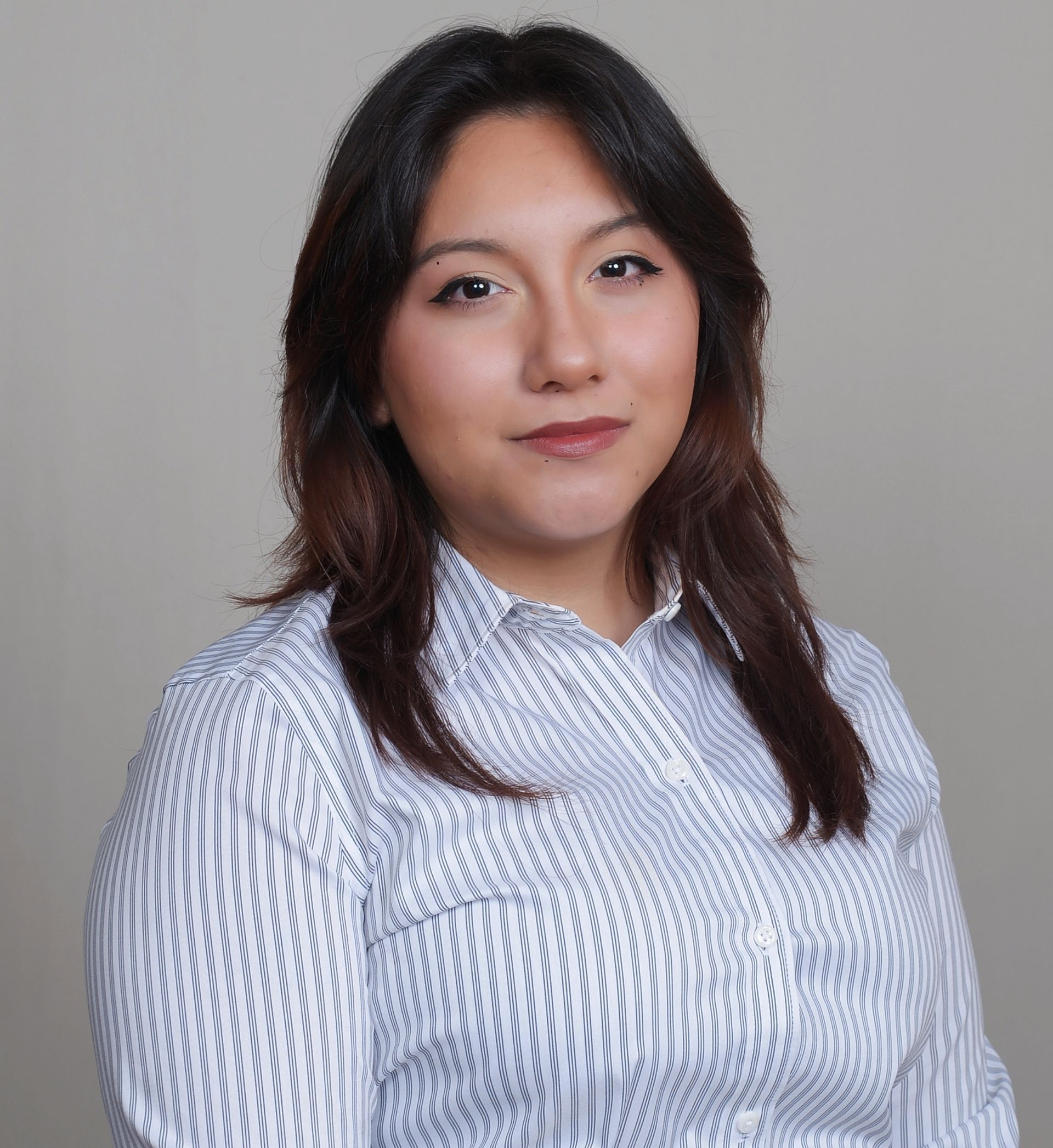Woman with dark hair in a striped button-up shirt smiling at the camera against a neutral backdrop.
