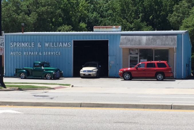 A blue auto repair shop building with a green truck, a silver sedan, and a red SUV parked in front on a sunny day. | Sprinkle and Williams II, Inc.