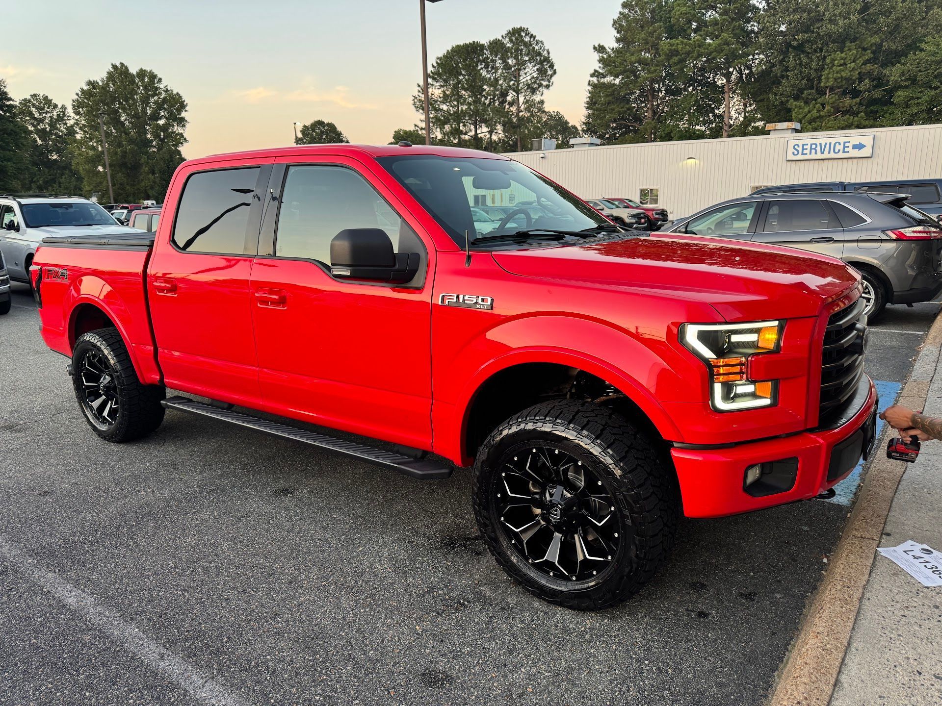 A bright red Ford F-150 pickup truck with black custom wheels and tinted windows parked in an asphalt parking lot.