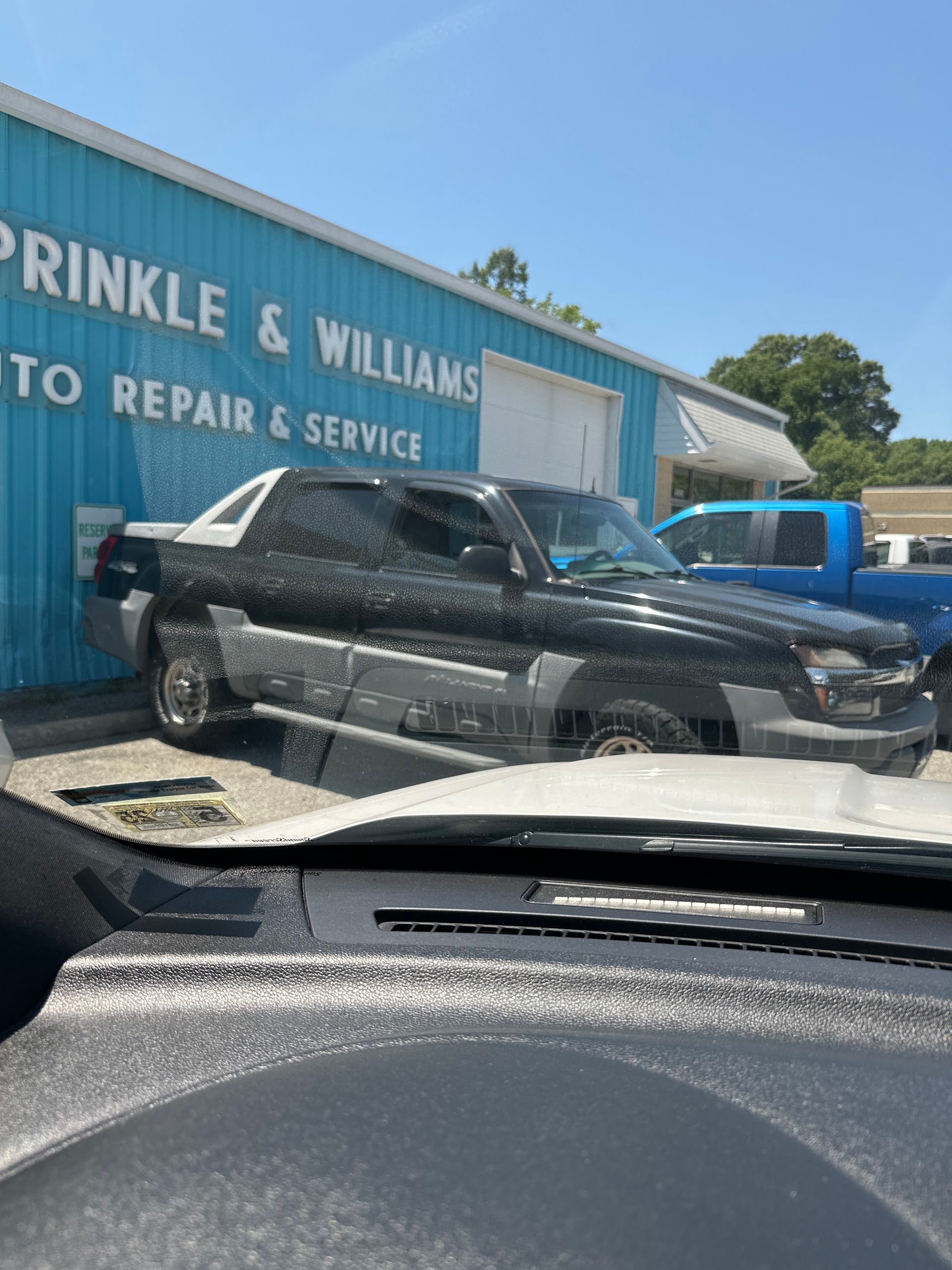 A black and grey Chevrolet Avalanche parked in front of a blue auto repair shop building. | Sprinkle and Williams II, Inc.