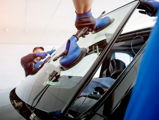 Two workers installing a car windshield using suction cups, indoors.